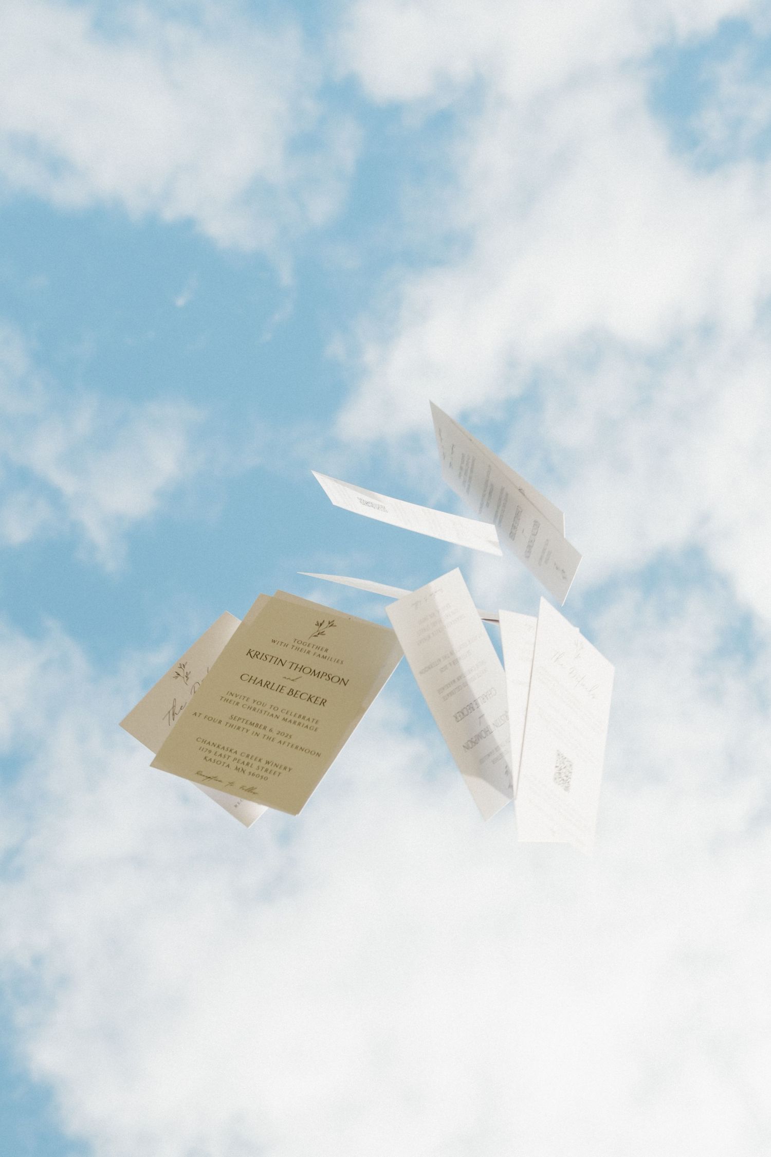 Paper airplanes with attached brown tags soar against a bright blue sky with white fluffy clouds.
