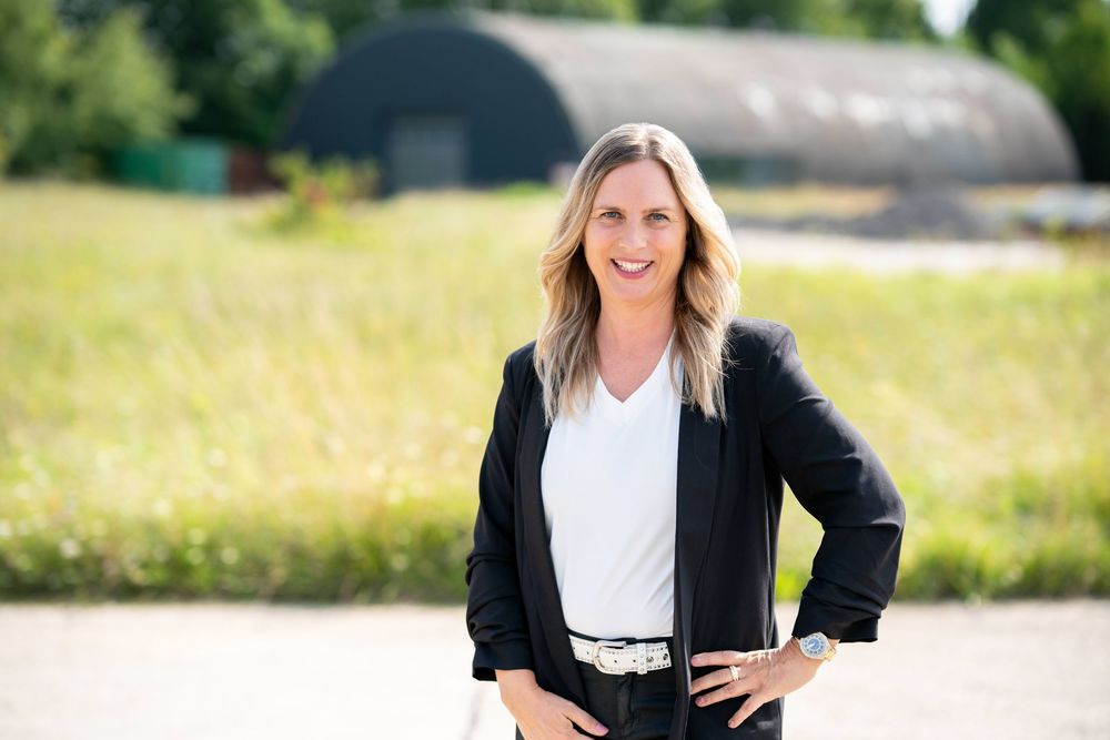 Professional outdoor business portrait of a person in a black blazer and white top smiling against a natural background.
