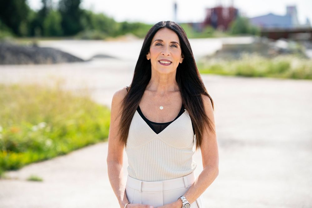 Business professional in white sleeveless top poses confidently outdoors on a bright day.