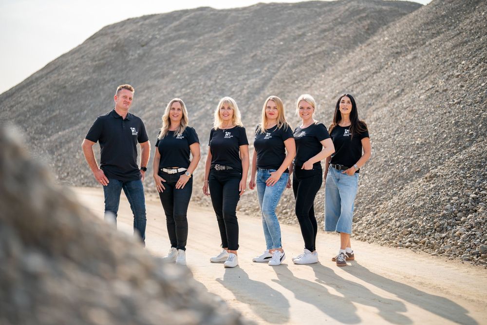 A group of people wearing black shirts stand together on a rocky hillside path in natural lighting.