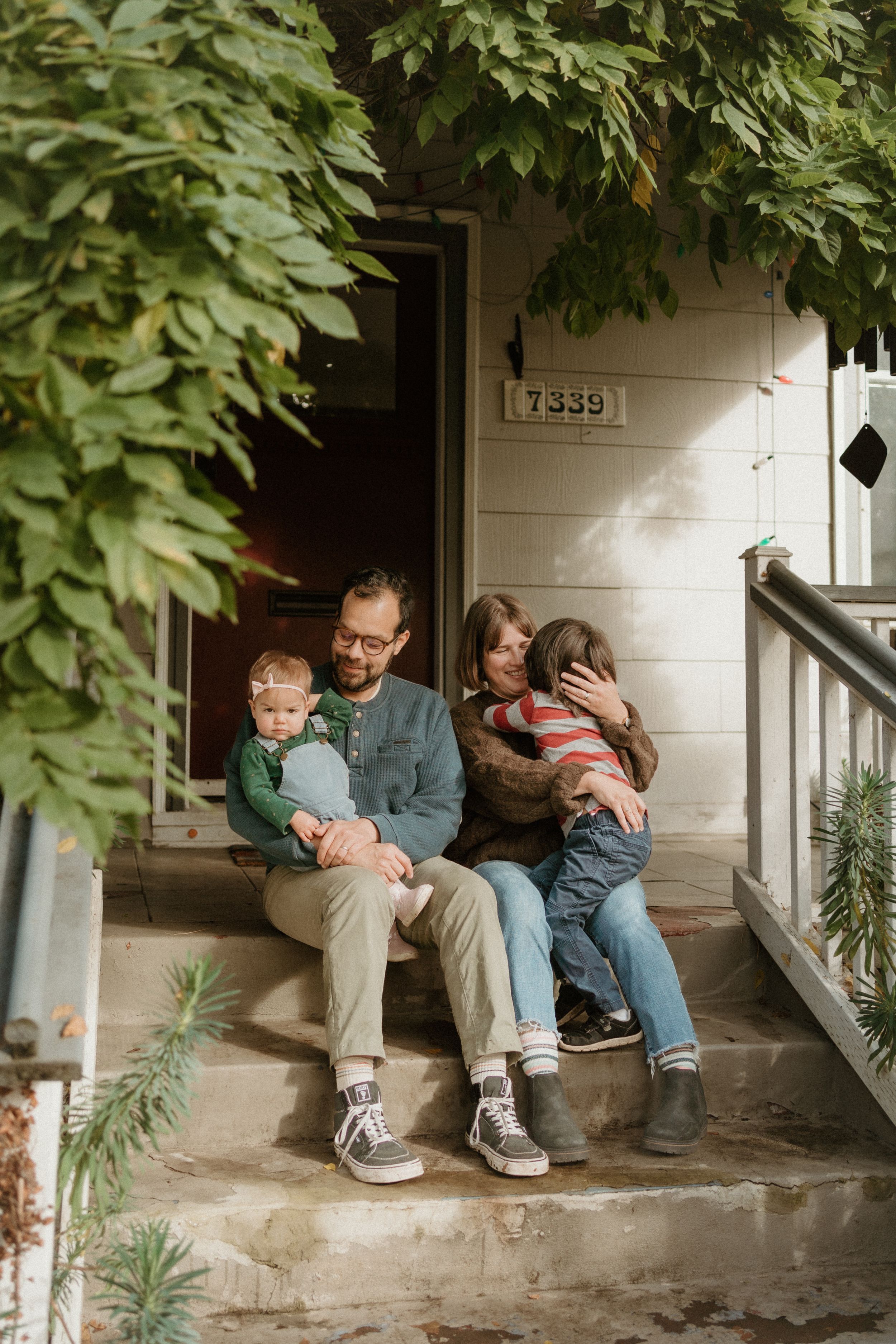 Candid family moment on porch steps with leafy backdrop.