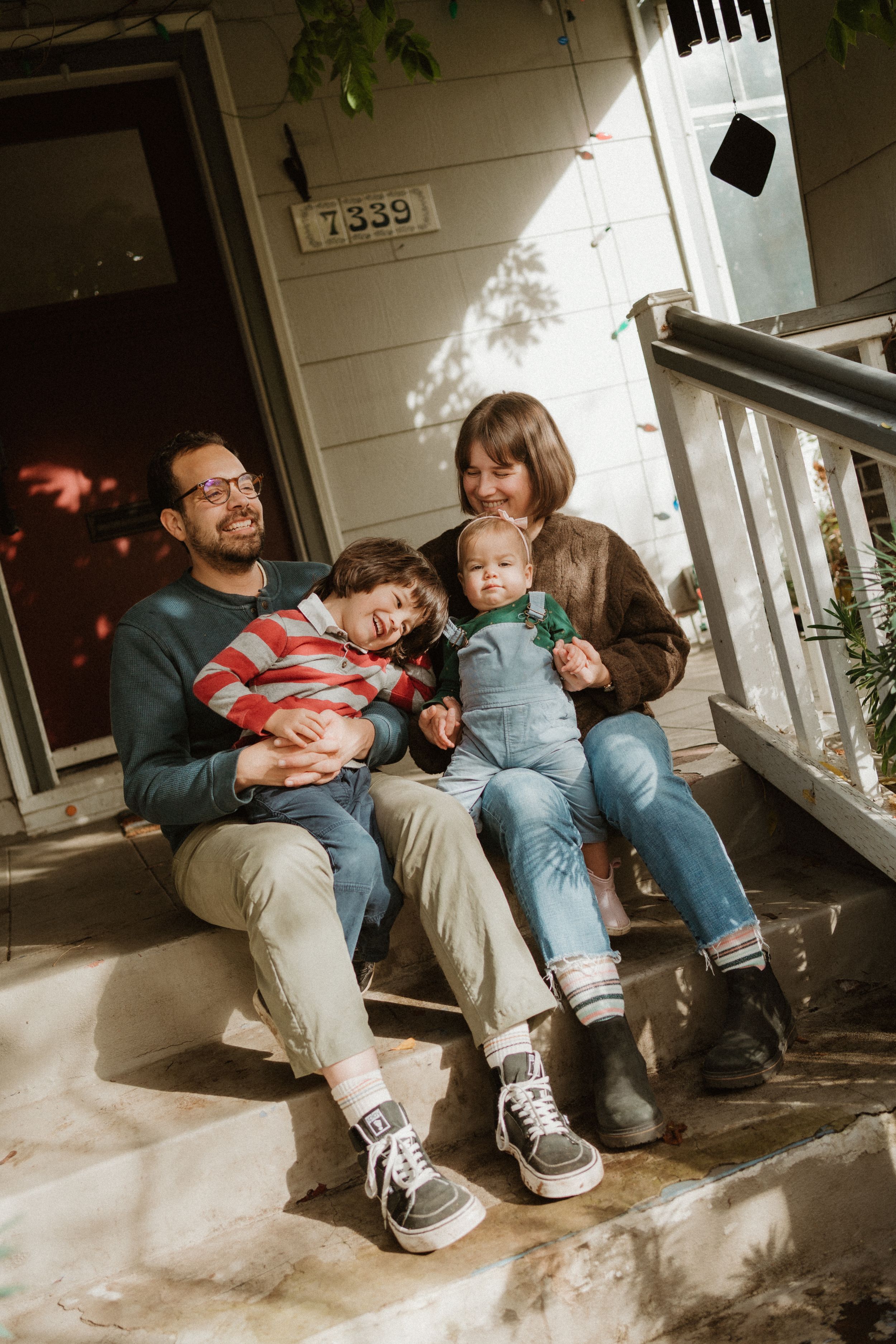 Relaxed family gathering on concrete porch steps in sunlight.