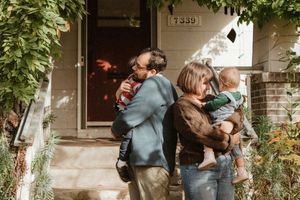A playful family moment captured outside their home entrance with greenery and brick details.