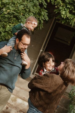 Warm family moment captured outside home entrance with leafy backdrop.