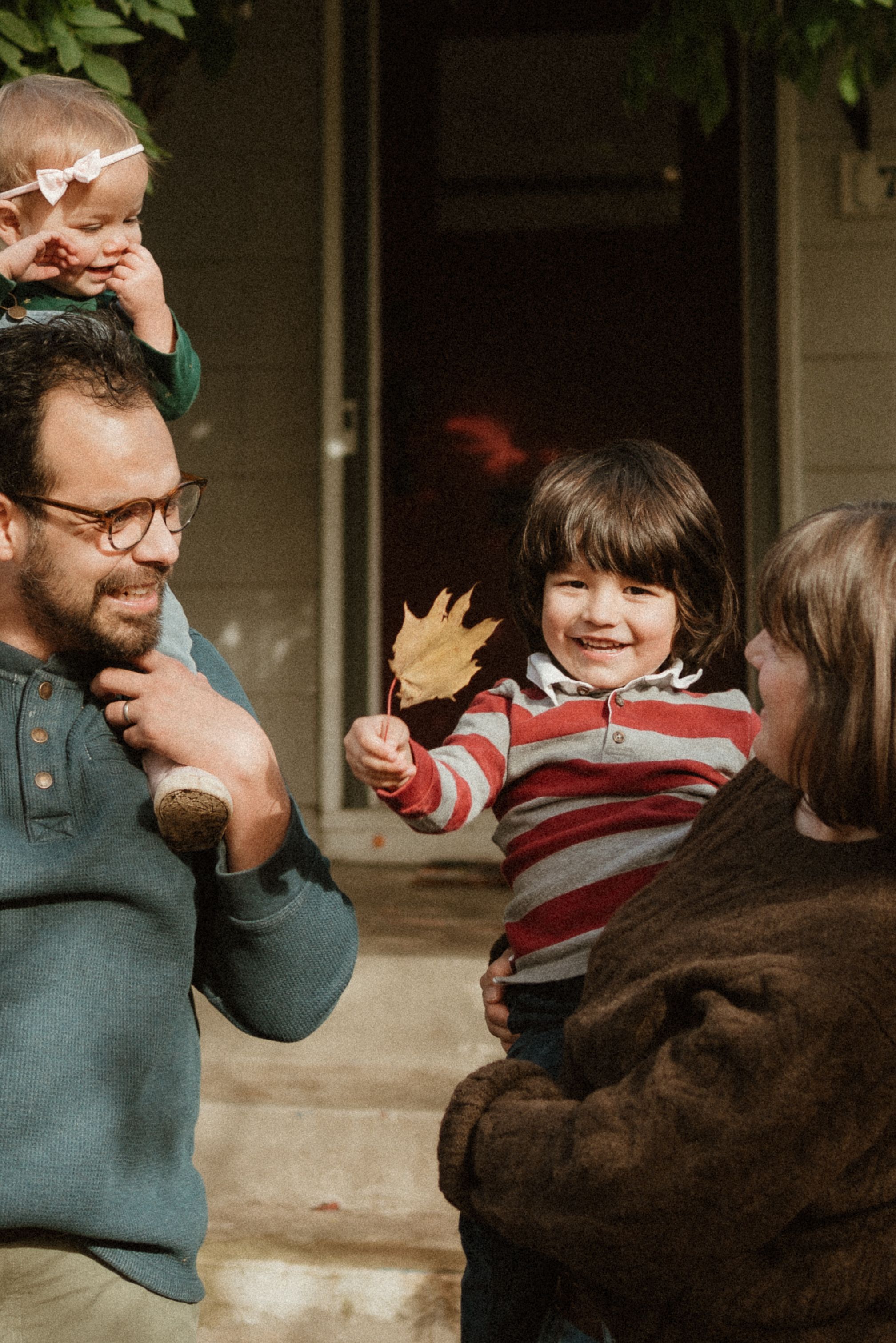 Candid family interaction filled with laughter outside brick home entrance.