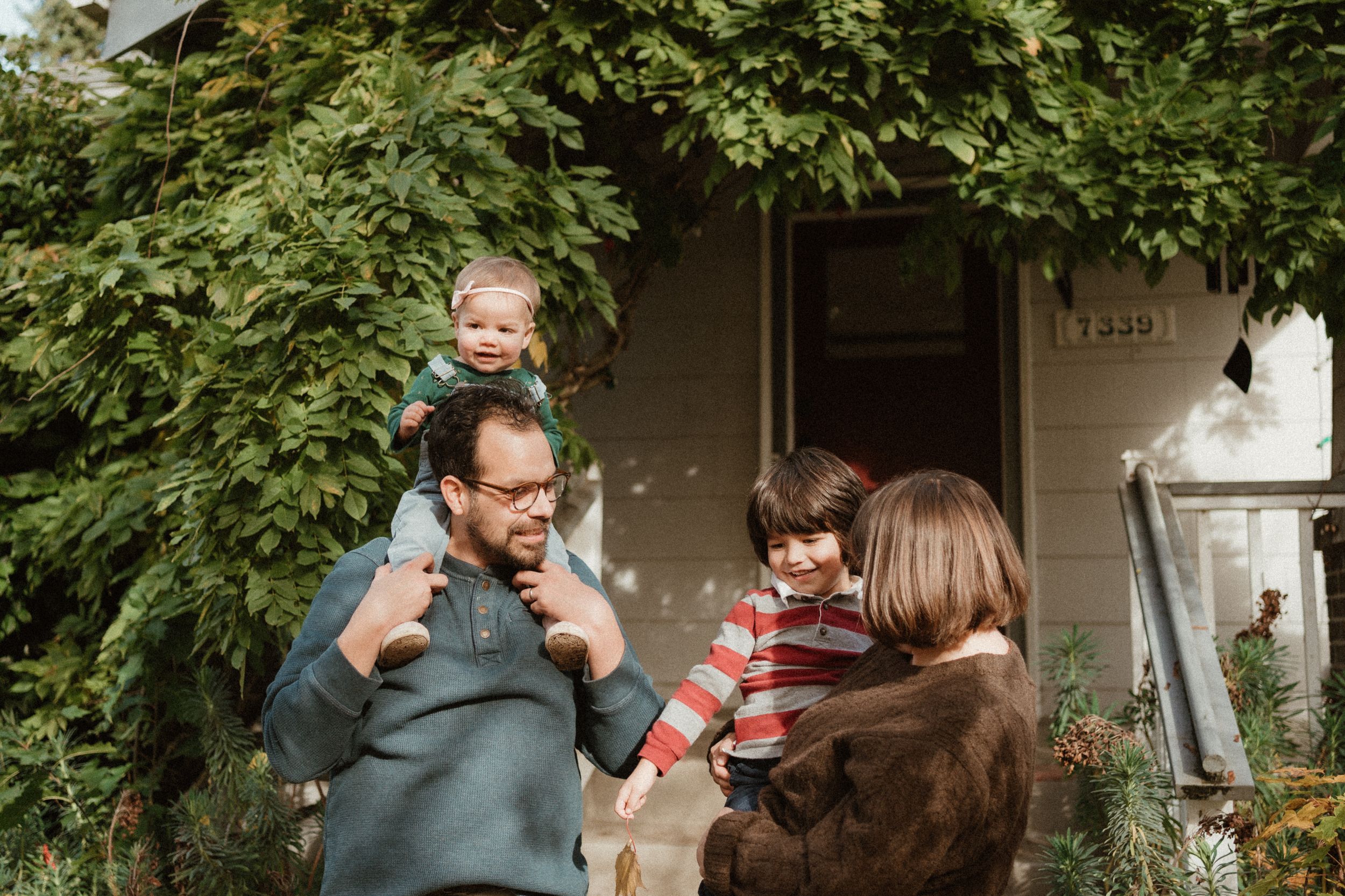 Family enjoying playful moments together on their front porch with green foliage overhead.