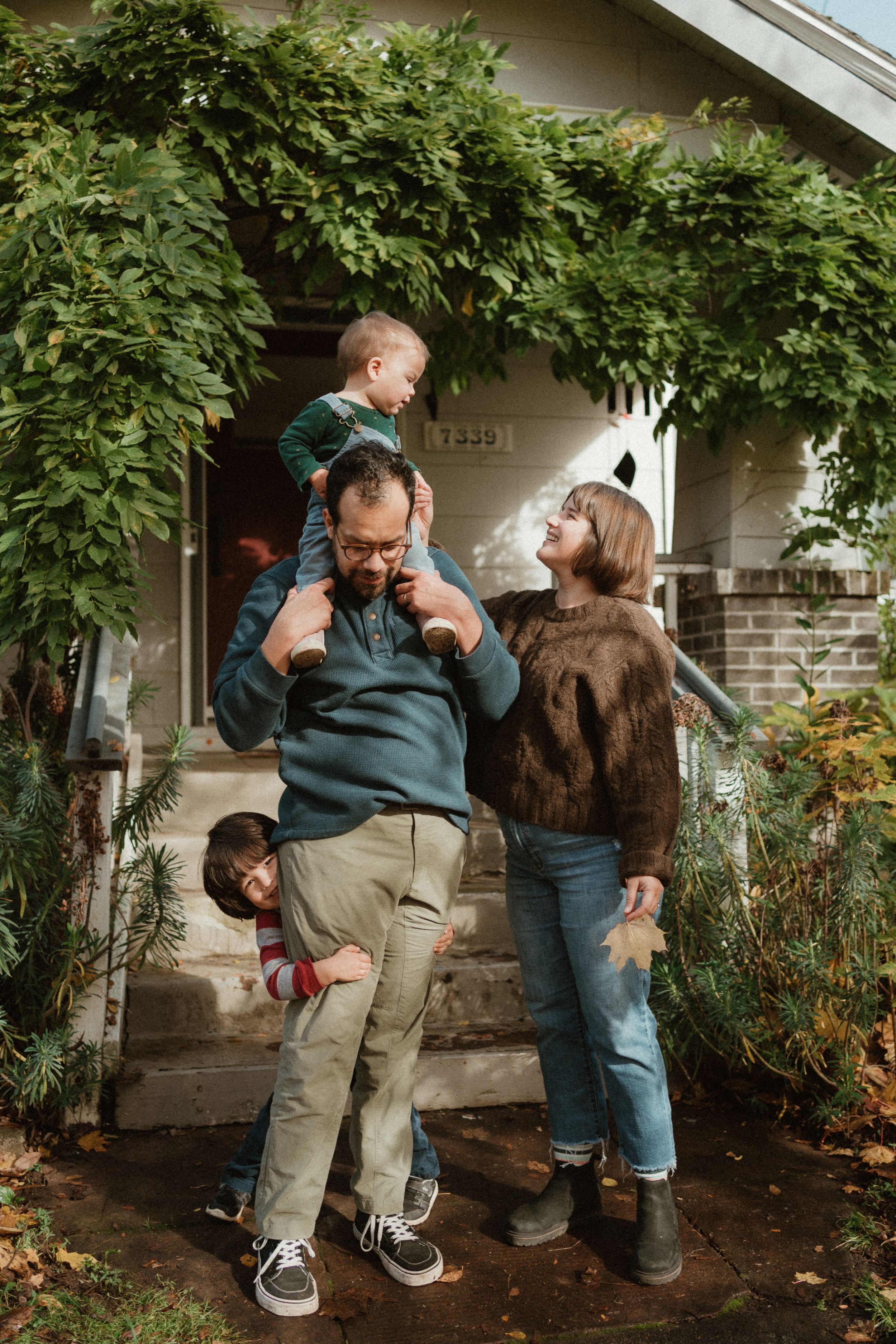 Dynamic family interaction captured on front steps with overhanging greenery.
