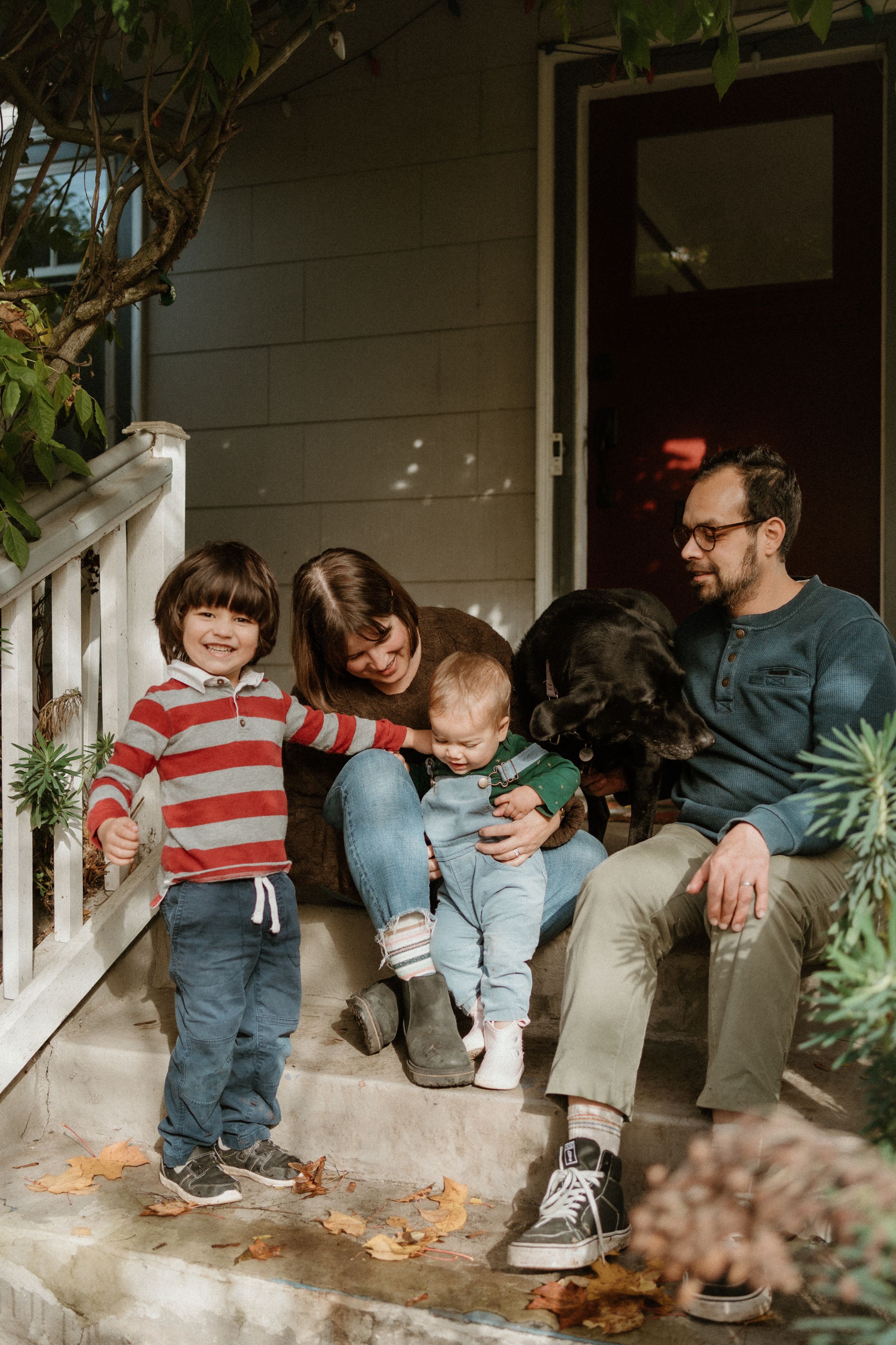 Family gathering on weathered porch steps with fallen leaves and natural lighting.