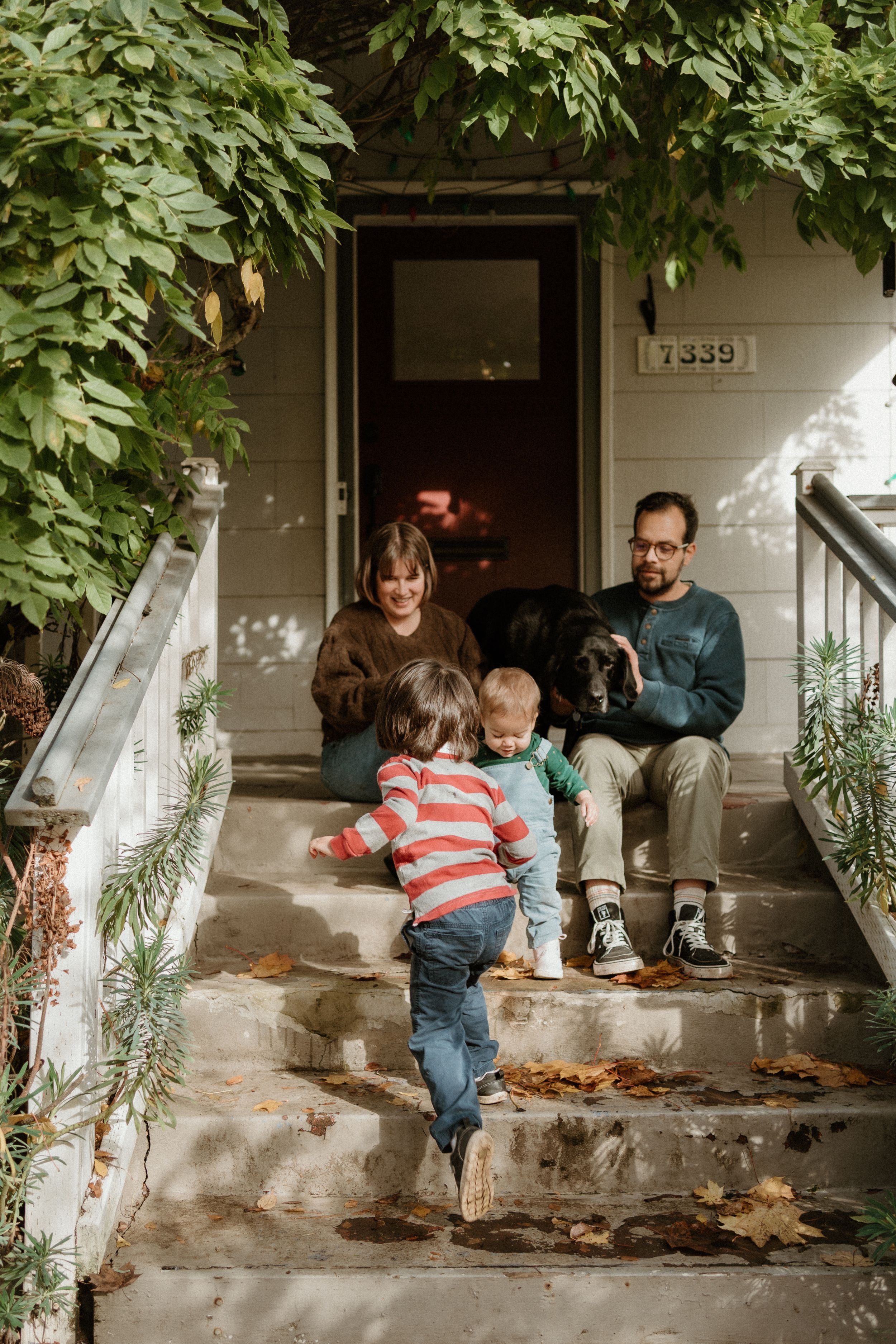 Casual family scene on rustic front porch steps with green foliage overhead.