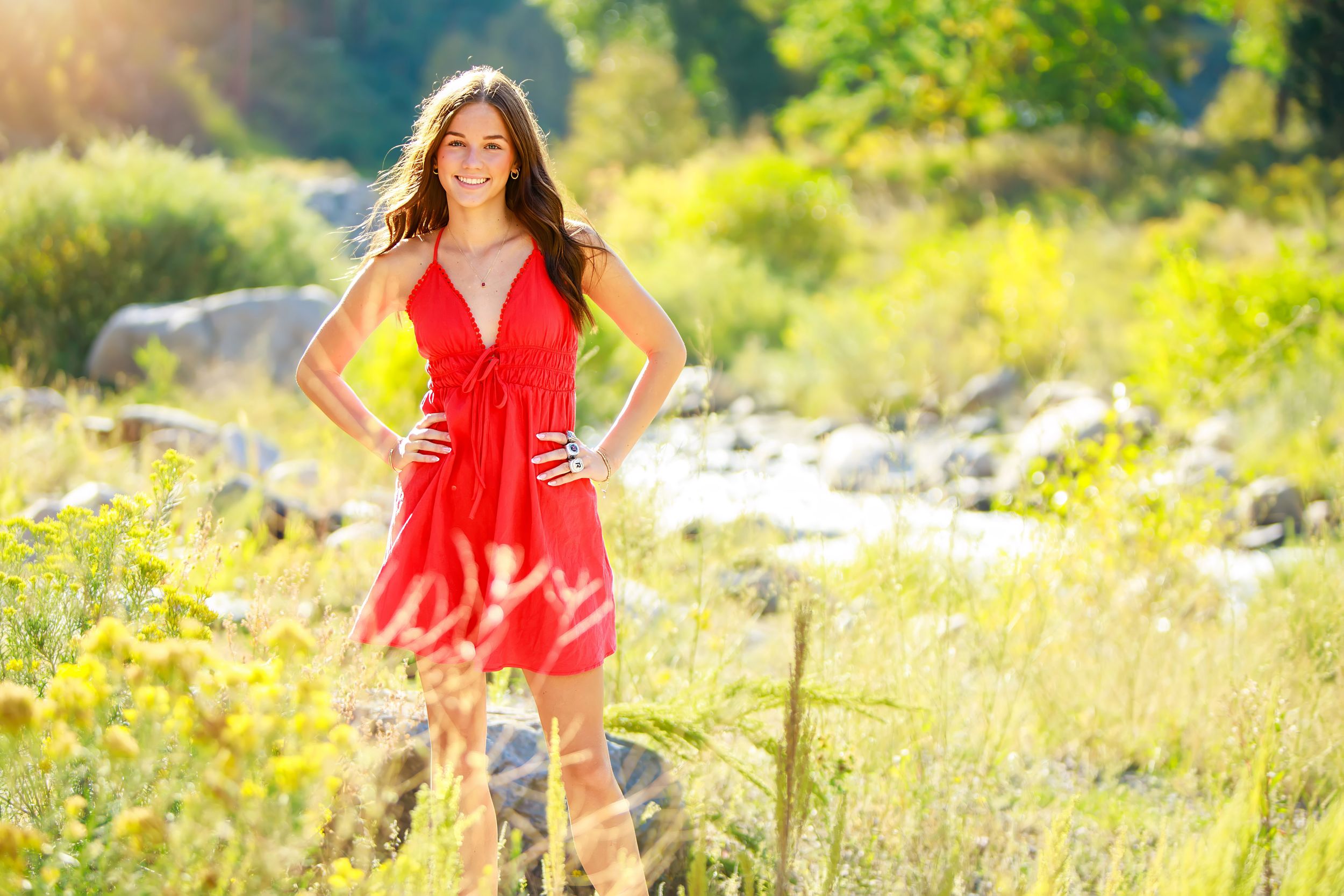 A bright red dress stands out against a sunlit meadow with wildflowers and natural scenery.
