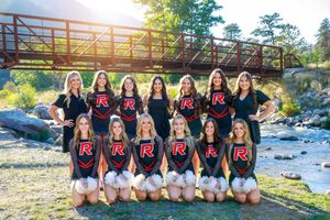 High school cheerleading squad posing outdoors near a bridge and river in matching black and red uniforms.