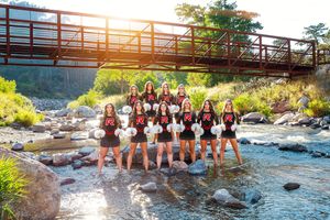 Cheerleading squad poses in river with bridge backdrop wearing black and red uniforms.