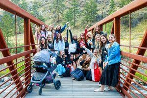 Large group of young women posing together on a red bridge surrounded by mountain scenery.