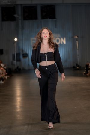 Model walks runway in black crop top and flared pants at Columbia Fashion Week show.