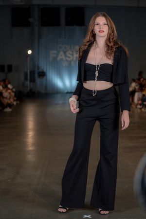 Fashion model showcases black ensemble with crop top and wide-leg pants on runway.