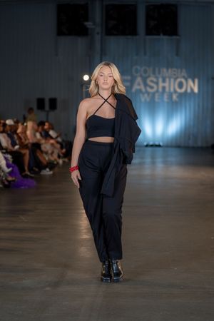 Model showcases all-black ensemble with dramatic draping on illuminated fashion runway.