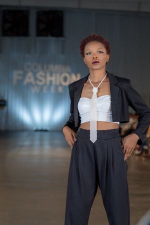 Runway model presents navy business suit with white crop top at fashion show.