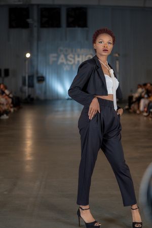 Professional model showcases navy business suit with cropped white top on fashion runway.