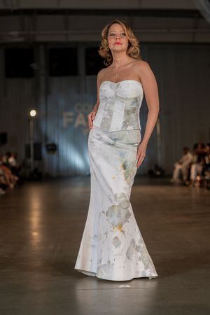 Elegant white floral mermaid gown with strapless bodice shown on runway at fashion show.