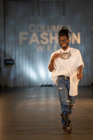 Model walks runway in casual white t-shirt, ripped jeans and statement necklace.