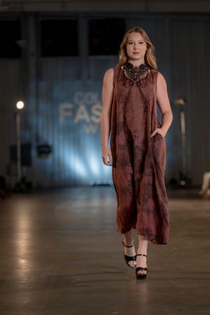 Burgundy sleeveless dress flows elegantly as model strides down fashion runway.