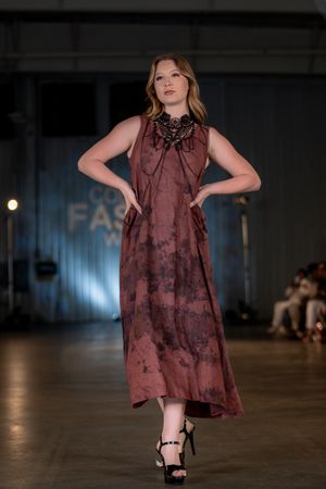 Model presents burgundy tie-dye maxi dress with statement necklace on fashion runway.