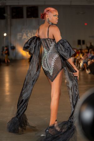Dramatic black bodysuit with flowing cape sleeves and sequin details shown from behind on runway.