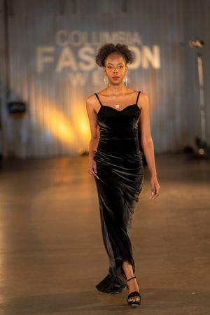 Black velvet evening gown displayed during fashion show with warm ambient lighting.