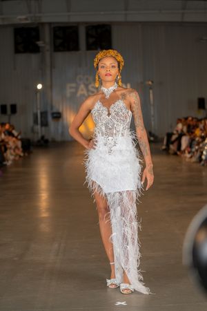 A model walks the runway in a white feathered dress with halter neckline at a fashion show.