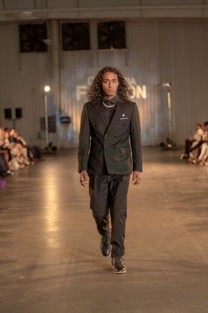 Dark suit with tailored blazer and trousers styled with casual elegance on fashion runway.