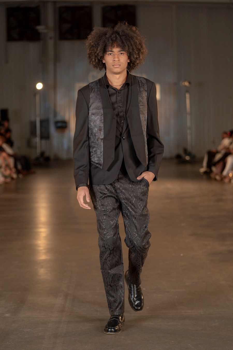 Modern black suit with textured panels and relaxed fit presented at fashion show.
