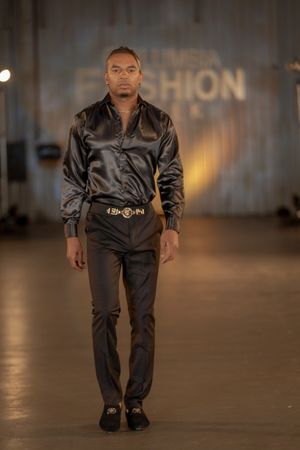 A model wears a sleek black satin shirt with matching pants on the Columbia Fashion Week runway.