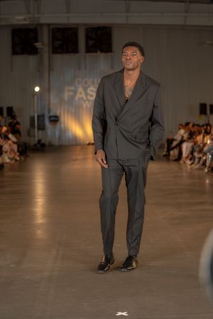 Model walks runway in charcoal grey suit at Columbia Fashion Week show.