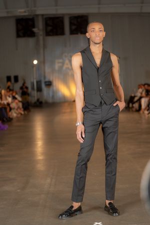 Model walks runway in sleek dark vest and pants ensemble at fashion show.