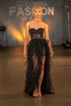 Dramatic black tulle evening gown with corset bodice and high slit shown on fashion runway.