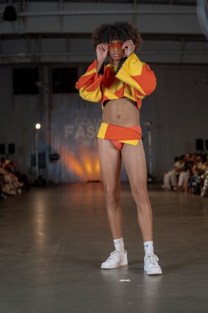 Dancers in yellow and orange costumes perform on stage wearing white sneakers during a fashion show performance.