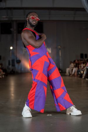 Bold geometric print jumpsuit in red and purple with white sneakers shown at fashion show.