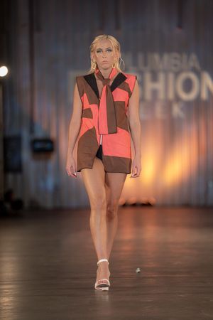 Model presents coral and brown color-block sportswear with white shoes on runway.