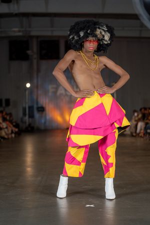Model poses in bold pink and yellow avant-garde design with white boots on runway.