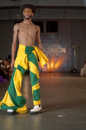 Model walks runway in yellow and green statement pants with white sneakers.