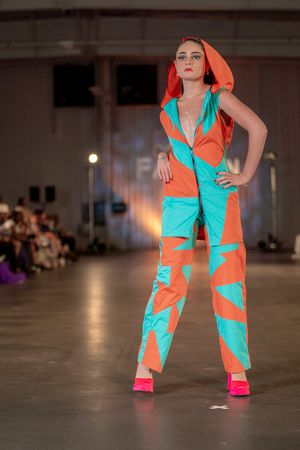 Model showcases bold orange and turquoise colorblock jumpsuit with matching headpiece.