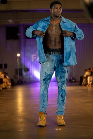 Model walks runway in matching light blue denim jacket and jeans with yellow boots during fashion show.