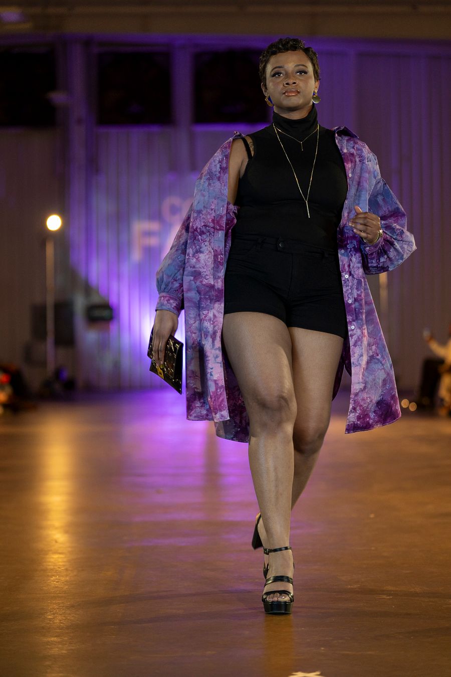 A dancer in a black outfit and floral kimono performs on stage under purple lighting.