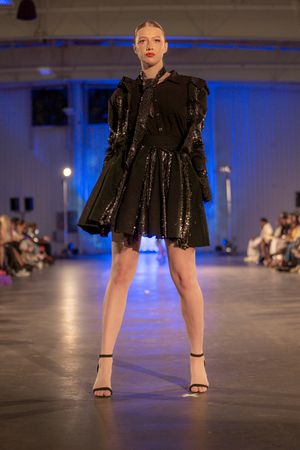 Model showcases sparkly black cocktail dress with structured shoulders on runway.
