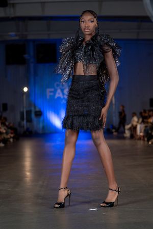 Black fringe mini dress with delicate straps showcased on illuminated catwalk.