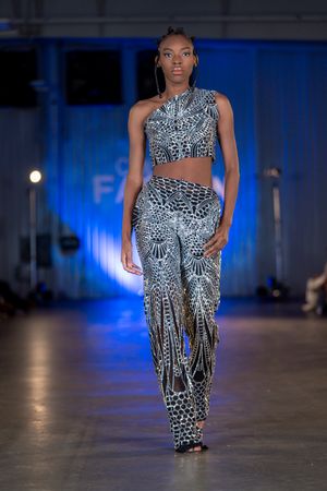 Model presents fitted geometric print ensemble in black and white on blue-lit runway.