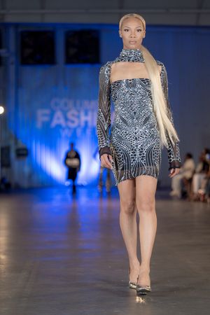 Model walks runway in shimmering silver beaded cocktail dress with long sleeves during fashion show.