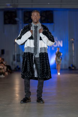 Model showcases black and white striped outfit with fur coat on illuminated runway.