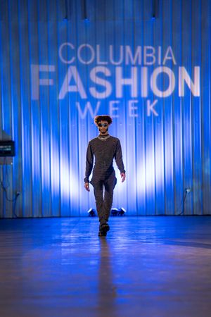 Model walks dimly lit runway with blue lighting at Columbia Fashion Week.