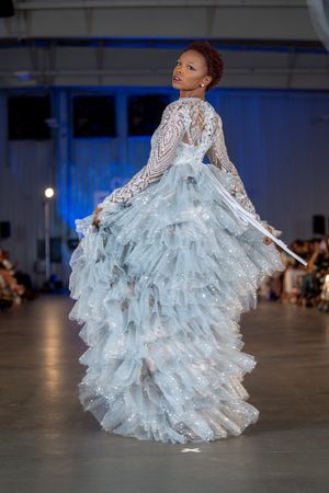 Dramatic white lace wedding gown with tiered ruffles shown from back angle on runway.